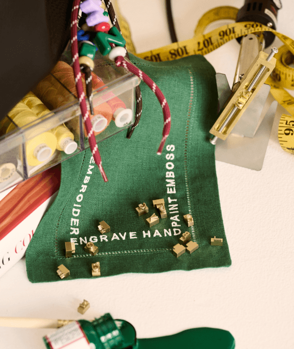 Embroidery workspace with green linen, gold letter stamps, and thread spools